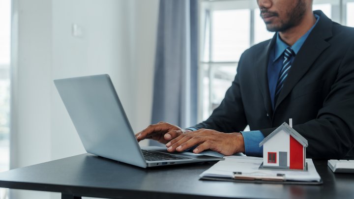 Mixed race asian indian man realtor chinese people find off-market real estate deals like a pro with house model in formal suit in office at desk